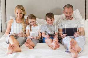 Parents and kids using mobile phone and digital tablet on bed