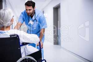 Male doctor interacting with senior patient on wheelchair in the corridor