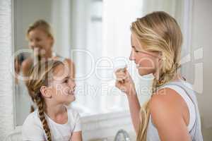 Mother interacting with daughter while applying a lipstick in bathroom
