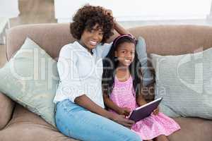 Mother and daughter sitting on sofa using digital tablet at home