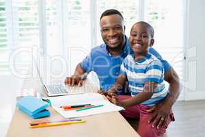 Portrait of father using laptop and son doing his homework