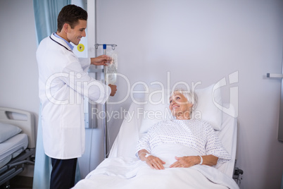 Doctor adjusting iv drip while patient lying on bed