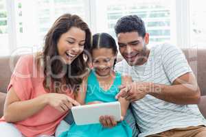 Parents and daughter using digital tablet in living room