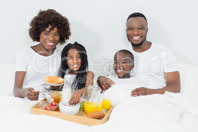 Portrait of smiling parents and kids having breakfast in bedroom