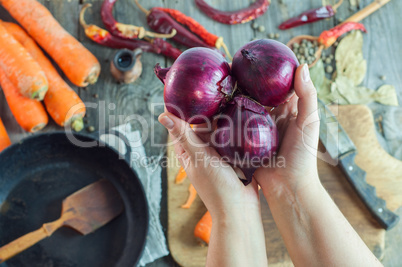 female hands holding three red onions on the background of the t