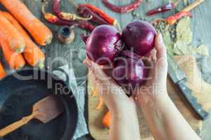 female hands holding three red onions on the background of the t