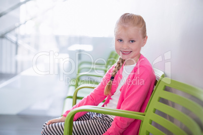 Portrait of smiling girl sitting on chair in corridor