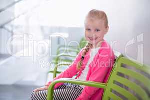 Portrait of smiling girl sitting on chair in corridor