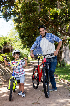 Portrait of father and son standing with bicycle in park