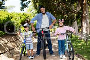 Portrait of father and children standing with bicycle in park