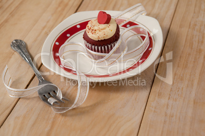 Plate with delicious cupcake decorated with a ribbon and fork