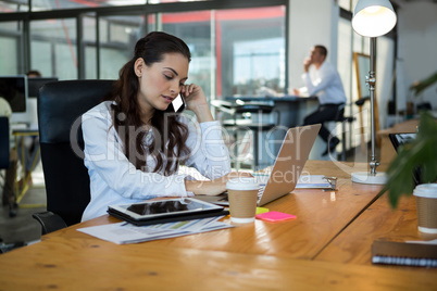 Business executive talking on mobile phone while using laptop at desk