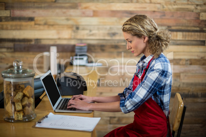 Waitress sitting at counter and using laptop in cafÃ?Â©
