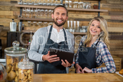 Smiling waiter and waitress using digital tablet at counter in cafe