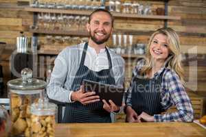 Smiling waiter and waitress using digital tablet at counter in cafe