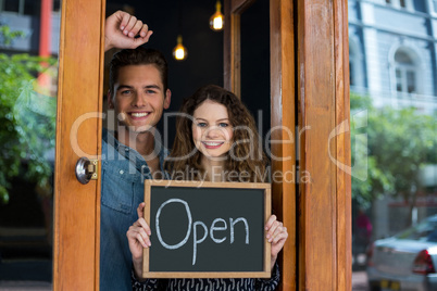 Portrait of man and woman showing chalkboard with open sign