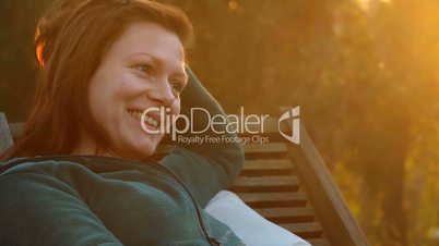 Young beautiful thinking woman with beauty patch on her cheek relaxs on a deck-chair in sunset back light looking into the distance