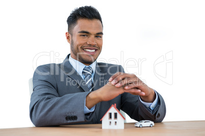 Smiling businessman protecting house model and car with hands