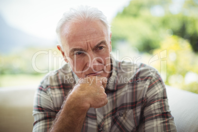 Thoughtful senior man sitting on sofa in living room