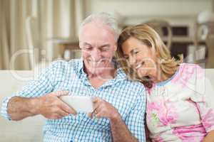 Smiling senior couple reviewing captured photos on mobile phone in living room