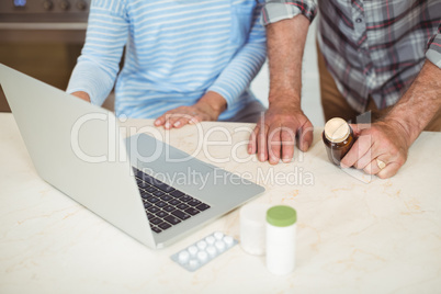 Senior couple holding medicine bottle and using laptop
