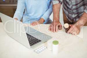 Senior couple holding medicine bottle and using laptop