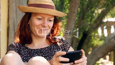 Woman relaxes in the garden enjoying her smartphone in the sun