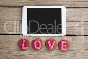Digital tablet with cookies displaying love message on wooden surface