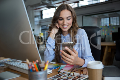 Female graphic designer using mobile phone at desk