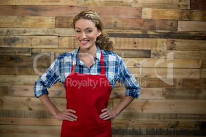Portrait of smiling waitress standing with hand on hip against wooden wall