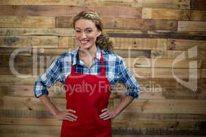 Portrait of smiling waitress standing with hand on hip against wooden wall