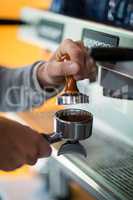 Waiter using a tamper to press ground coffee into a portafilter