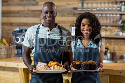 Portrait of waiter and waitress holding a plate of cupcake and croissant