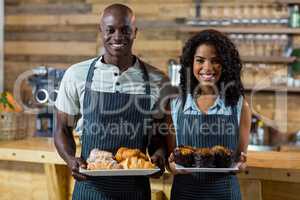 Portrait of waiter and waitress holding a plate of cupcake and croissant