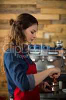 Waitress using a tamper to press ground coffee into a portafilter