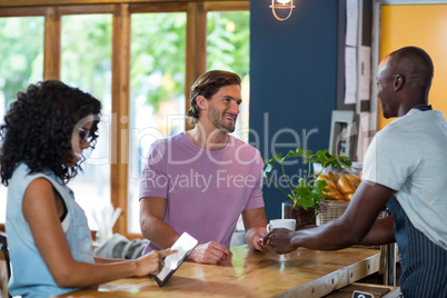 Waiter serving coffee to man while woman using digital tablet at counter