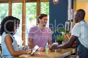 Waiter serving coffee to man while woman using digital tablet at counter