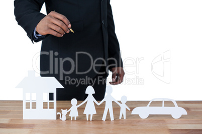 Mid section of businessman with paper cut out family, house and car at desk