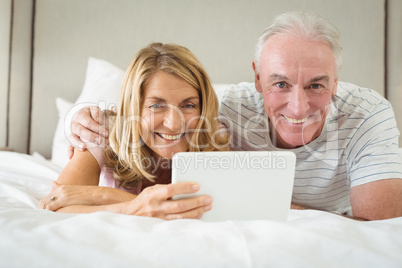 Portrait of smiling couple lying on bed and using laptop