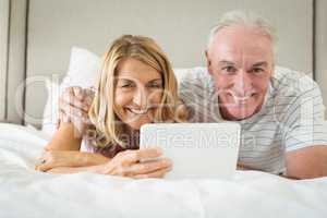 Portrait of smiling couple lying on bed and using laptop