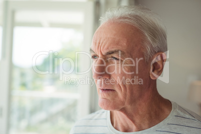 Thoughtful senior man standing next to window