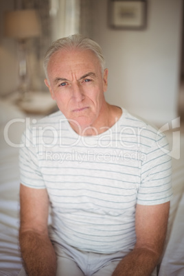 Portrait of senior man sitting on bed in bedroom