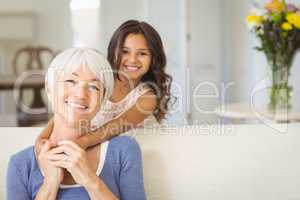 Portrait of smiling granddaughter embracing her grandmother in living room
