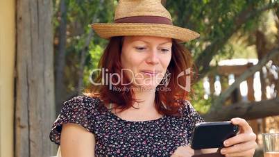 Woman sits in the garden enjoying her smartphone in the sun