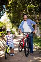 Portrait of father and son standing with bicycle in park