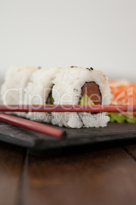 Uramaki and sashimi sushi served with chopsticks in black stone slate