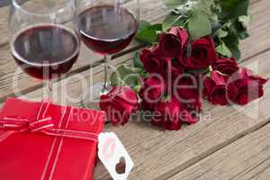 Red wine glasses, gift and roses on wooden surface