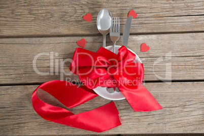 Cutlery and white plate tied up with red ribbon