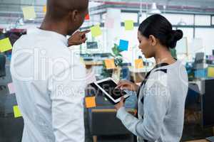 Business colleagues using digital tablet while discussing over sticky notes on glass