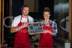 Smiling waitress and waiter standing with open sign board outside cafÃ?Â©